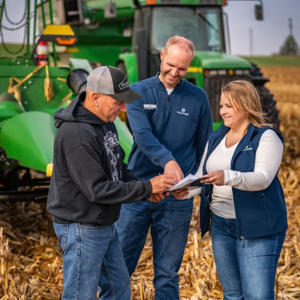 Three Hills Bank agricultural services team members review a clipboard beside a tractor.