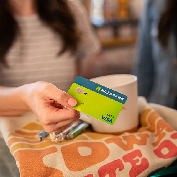 A hand holding a Hills Bank debit card.