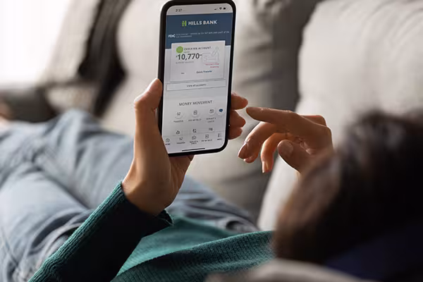 Person laying on a couch checking Hills Bank mobile app.