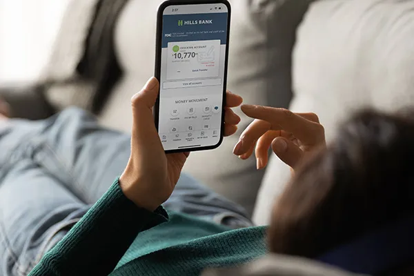 Person laying on a couch checking Hills Bank mobile app.